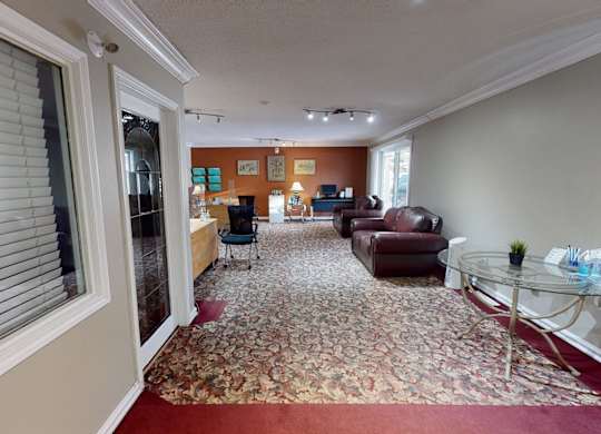 A welcoming community lounge here at Cambridge West with patterned carpet, comfortable leather seating, and a bright open layout, featuring a business center area with desks, computers, and warm accent walls.