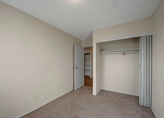 A cozy bedroom here at Cedar Gardens with soft carpeting and a bright, neutral color palette, featuring a spacious closet with sliding doors, an open layout for easy furniture placement, and a simple design that feels calm and comfortable.