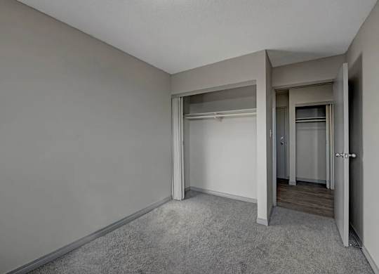 A bright bedroom here at Cedar Gardens with soft gray carpeting and clean, neutral walls, featuring a roomy open closet, a convenient hallway connection, and a simple layout that feels comfortable and easy to make your own.