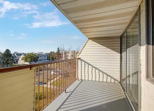A sunny balcony here at Cedar Gardens with a covered outdoor space and sturdy railing, featuring an open layout with room for a small seating set, warm natural light, and relaxing neighborhood views for an easy spot to unwind.