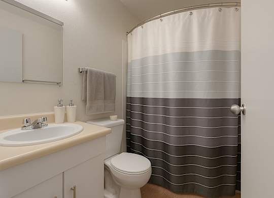 A clean bathroom here at Cedar Gardens with a bathtub-shower combo and a modern striped shower curtain, featuring a light vanity with a smooth countertop, a bright mirror, and soft towel accents for a fresh, comfortable feel.
