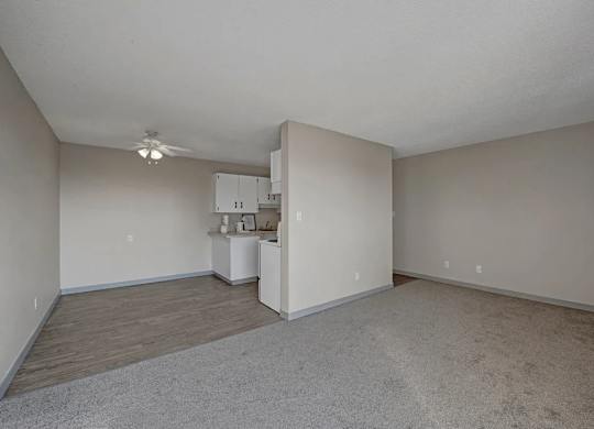 A spacious living area here at Cedar Gardens with an open layout and soft neutral tones, featuring plush carpeting, a separate dining nook with durable flooring, and a ceiling fan overhead for a comfortable, airy feel.