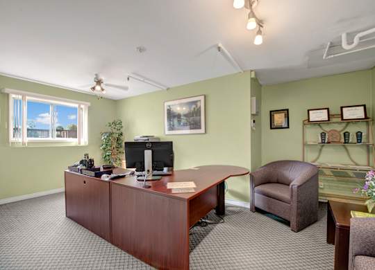 A welcoming on-site office here at Gateway Square with soft green walls, a large wooden desk, comfortable seating, framed artwork, and bright lighting creating a professional and inviting atmosphere.