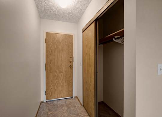 A bright entryway here at Gateway Square featuring a clean tiled floor, warm wood-toned front door, and a spacious closet for easy storage, creating a simple and welcoming first impression.
