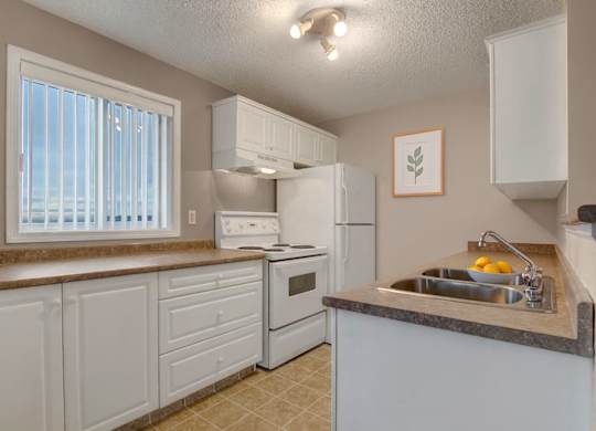 A bright kitchen here at Pointe at Applewood with white cabinets, brown countertops, and a double stainless steel sink. A window with vertical blinds brings in natural light, with a full appliance set and a clean, inviting layout.