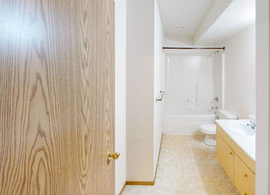 A clean, bright bathroom here at Quail Ridge with a bathtub-shower combo, light tile flooring, and a spacious vanity with a white countertop and sink. A built-in linen shelving area adds convenient storage for towels and everyday essentials.