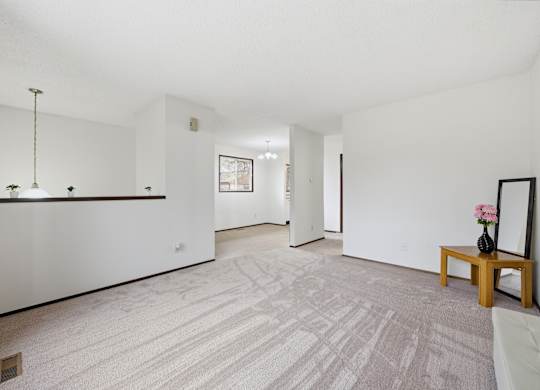 A room with a carpeted floor and a bench with a vase of flowers on it.