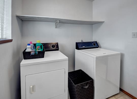 A convenient laundry area here at Willowview Terrace with a full-size washer and dryer, a wide storage shelf for supplies, and a nearby window that brings in natural light. A simple basket setup adds extra organization for everyday laundry needs.