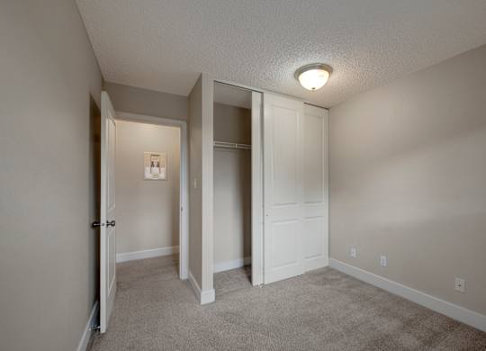 A simple bedroom here at Wyndham Crossing with soft neutral walls, plush carpet flooring, and a warm ceiling light for a comfortable layout. A sliding-door closet with hanging storage sits beside the open doorway leading into the hallway.