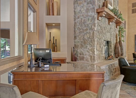 Cozy office here at Cheyenne Creek Apartment Homes with a wooden desk, computer, and lamp. Stone fireplace with decorative vases and greenery on the mantle creates a warm, inviting atmosphere.