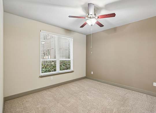A room with a ceiling fan and a window showing greenery outside.
