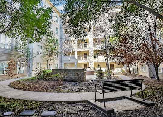 A bench sits in front of a building with a circular garden in the foreground.