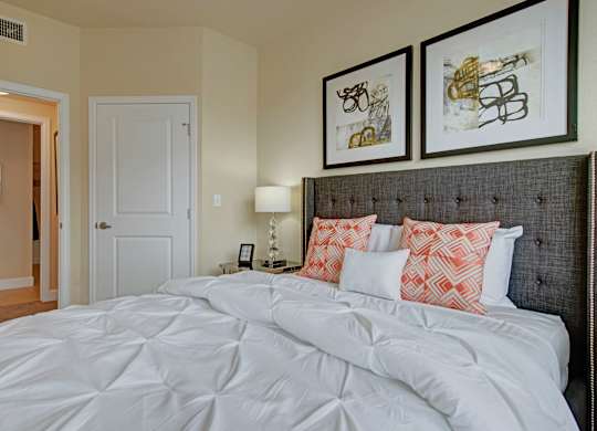 A bed with white sheets and pillows in a room with two framed pictures on the wall.