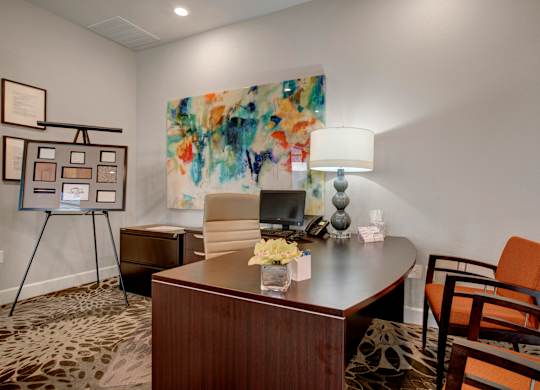 A room with a desk, chair, and painting on the wall.