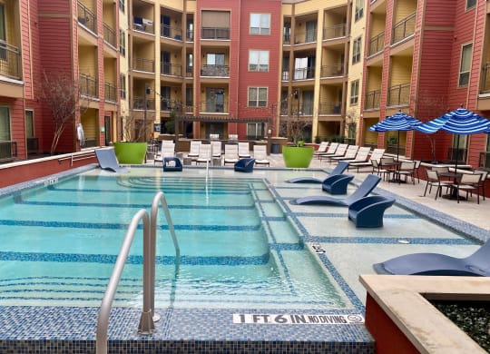 a swimming pool at an apartment building with chairs and umbrellas