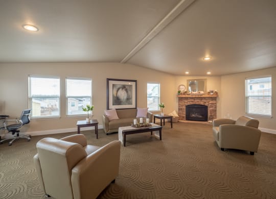 Spacious resident lounge here at Four Seasons Apartments with beige armchairs, a stone fireplace, large windows, abstract art, and patterned carpet, conveying a cozy and elegant ambiance.