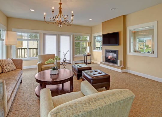 Cozy living room here at The Glen Apartments with a modern design. Features beige couches, a round wooden table, a fireplace, and large windows. A chandelier adds elegance.