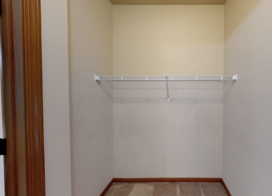 Empty beige closet here at Grand River Estates Apartment Homes with a wire shelf mounted on the back wall. The doorframe is wooden, and the floor is carpeted. Simple, tidy space.