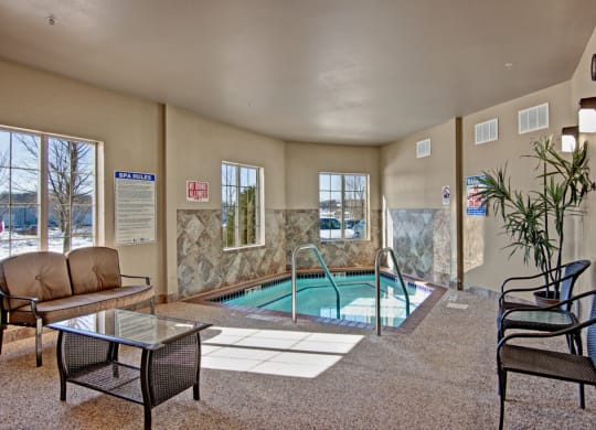 Cozy indoor spa room here at Grand River Estates Apartment Homes with a small pool, surrounded by four windows. There are chairs, a glass-top table, plant, and a warm, inviting atmosphere.