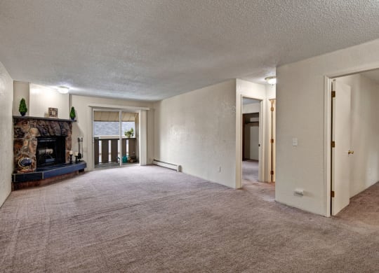 Spacious living room here at Greenbriar Apartments with light beige carpet, stone fireplace, sliding glass doors, and open doorways. Cozy and inviting with natural light.
