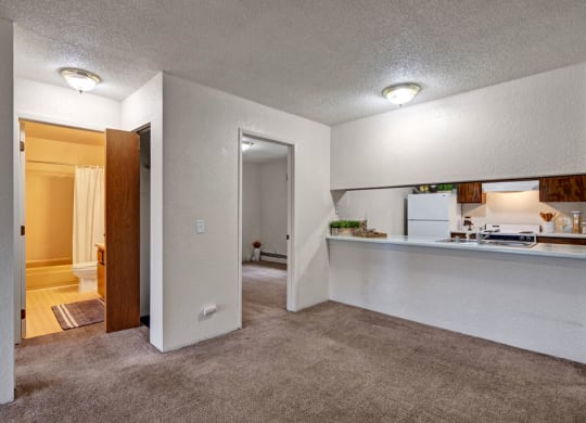 Cozy apartment interior here at Greenbriar Apartments with beige carpet and white walls. Features a small kitchen with a breakfast bar, bathroom with shower curtain, and softly lit rooms.