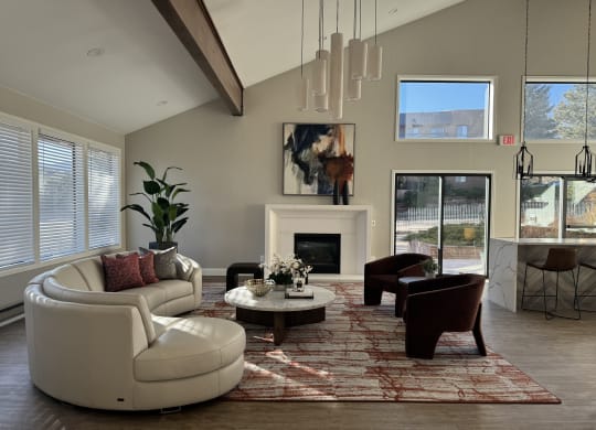 Spacious living room here at Eagle Ridge Apartment Homes with modern decor, featuring a white curved sofa and two brown chairs on a patterned rug. Large windows provide ample natural light.