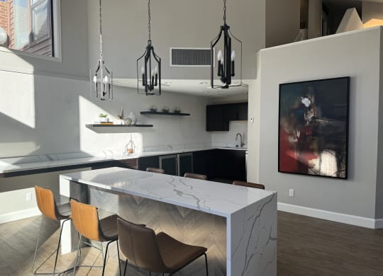 Modern kitchen here at Eagle Ridge Apartment Homes with a large marble island and four brown chairs. Three elegant black chandeliers hang above, with abstract art on a gray wall. Bright and inviting atmosphere.