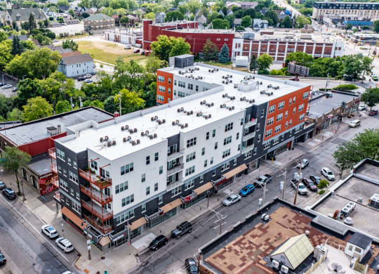 Aerial view of a Latitude Apartments featuring modern apartment buildings with white and orange facades. Surrounding greenery and parking lots can be seen, contributing to a tranquil urban atmosphere.