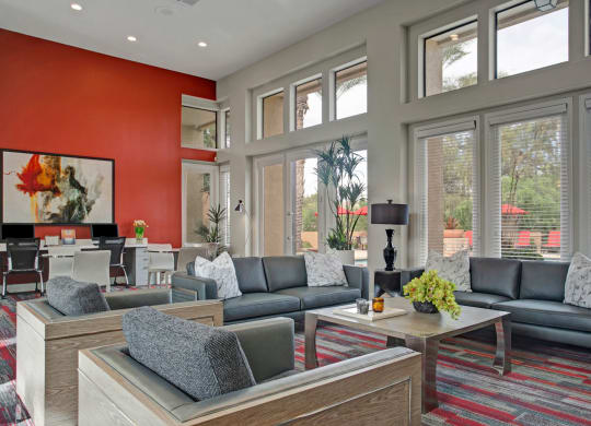 Modern lounge here at Mirador Apartments with gray sofas, patterned cushions, and a wooden coffee table topped with a plant. Red accent wall with abstract art and desks.
