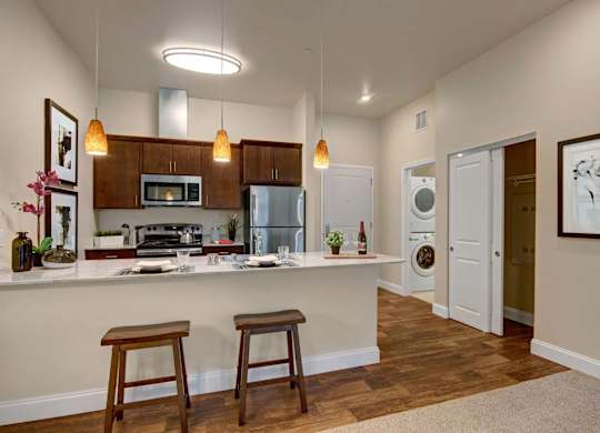 A modern kitchen here at 4800 Excelsior featuring dark wood cabinets, light countertops with bar seating, and pendant lighting above the breakfast bar. Stainless steel appliances, including a refrigerator, microwave, and range, are paired with warm wood-style flooring, while an in-home laundry area is visible just beyond the kitchen.