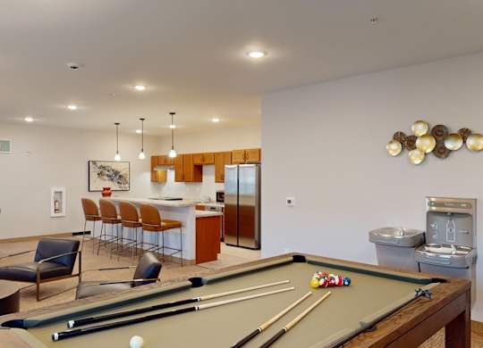 A community clubhouse here at Club at Heritage with a pool table, lounge seating, and a modern kitchen area. Pendant lighting, bar seating, and open space create a fun and inviting environment for gathering and entertainment.