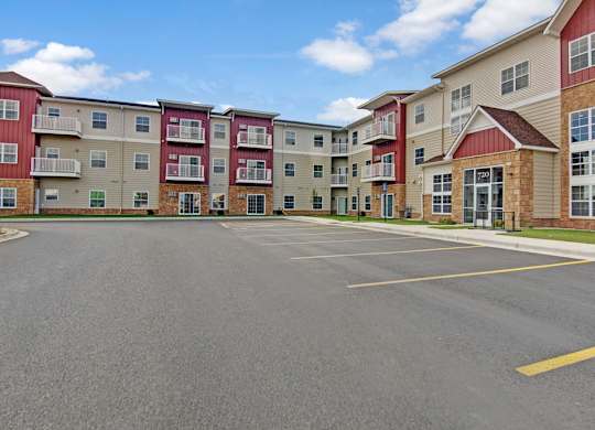 A community exterior here at Club at Heritage with multi-story buildings, private balconies, and a clean, spacious parking area. A welcoming entrance and modern design create a well-maintained and inviting atmosphere.