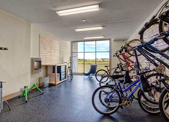 A functional bike storage and repair room here at Residence at the COR featuring wall-mounted bicycle racks, open floor space for maintenance, a repair station with tools and air pump, durable flooring, and large windows that bring in natural light while offering a convenient, organized area for cycling enthusiasts to store and tune their bikes.