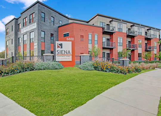 A Siena sign is in front of a building with a red and grey facade.