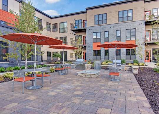 A patio with tables and chairs and umbrellas in front of apartment buildings.