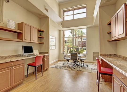 Modern office space here at Mozaic at Steele Park Apartments with wooden floors, large window, two workstations with computers, red chairs, and a round meeting table with rolling chairs. Bright and airy ambiance.