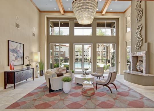 Luxurious resident lounge here at Mozaic at Steele Park Apartments with a high ceiling and large windows showcasing a pool view. Features modern furniture, abstract art, and an elegant chandelier.