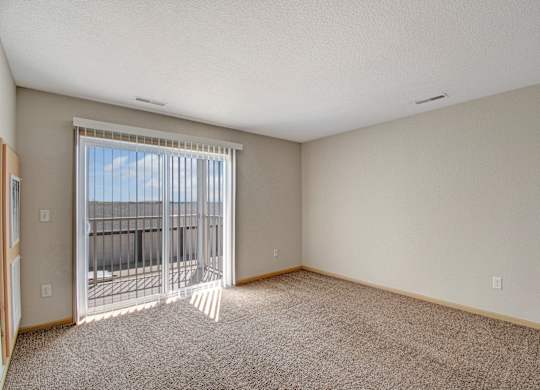 A room with a carpeted floor and a sliding glass door leading to a balcony.
