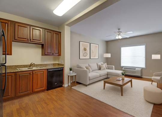 A bright open living room here at Prairie Vista featuring warm wood-look flooring, a modern neutral sectional sofa, coordinating accent chairs, a wooden coffee table, soft area rug, and an adjacent kitchen with rich cabinetry, creating an inviting and functional apartment layout.