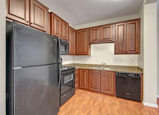 A bright kitchen here at Prairie Vista showcasing rich wood cabinetry, black appliances, granite-style countertops, wood-look flooring, and a functional L-shaped layout that offers ample storage and counter space for everyday cooking and entertaining.