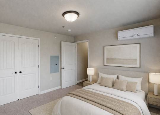 A bright, neutral bedroom here at Renaissance Heights featuring a comfortable bed with white bedding and beige accent pillows, matching bedside tables with lamps, soft carpet flooring, white double closet doors, and a wall-mounted air conditioning unit that creates a calm and inviting sleeping space.
