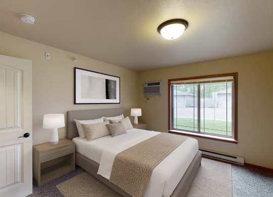 A cozy, well-lit bedroom here at Williston Garden Apartments with soft neutral walls, plush carpet, and a large window that brings in natural light and outdoor views. A neatly made bed with light bedding is paired with matching nightstands and lamps, while simple wall art and clean finishes create a calm, inviting atmosphere.