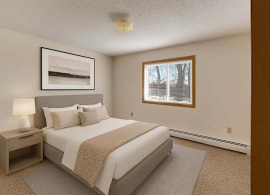 A calm, well-appointed bedroom here at Windscape Apartments featuring soft neutral walls, plush carpet, and a large window that provides natural light and outdoor views. A neatly styled bed with a padded headboard, coordinating nightstand, and simple artwork creates a comfortable, restful sleeping space.