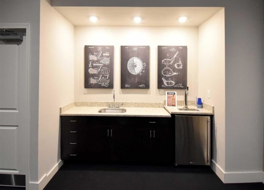 Small, well-lit kitchenette at the Oaks of Shorewood Apartments with granite countertops and dark cabinets. Above are three framed technical patent drawings, adding a modern, sophisticated touch.