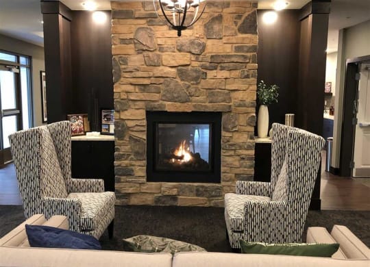 Cozy living room at the Oaks of Shorewood Apartments with stone fireplace, two patterned armchairs, a sofa with colorful cushions, and warm lighting, creating an inviting atmosphere.