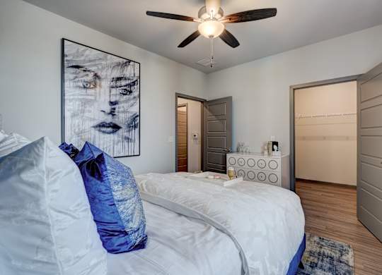 A bedroom with a bed, a ceiling fan, and a painting on the wall.