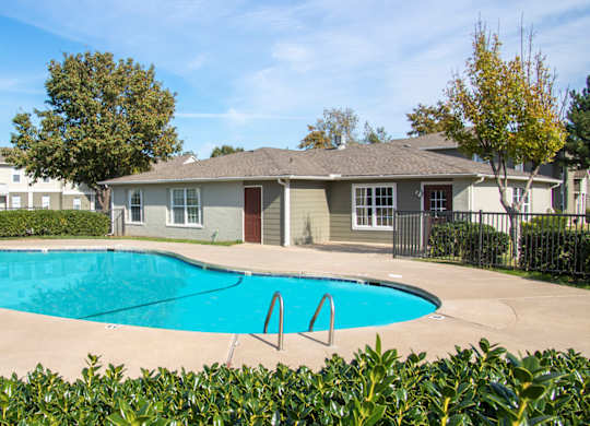 A swimming pool in front of a house with a fence around it.
