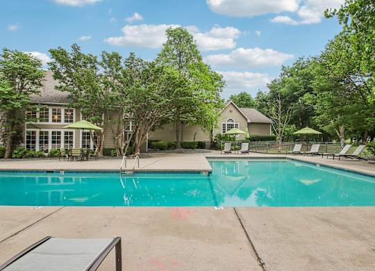 A swimming pool surrounded by trees and a house in the background.