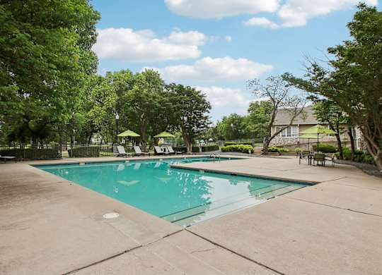 A large swimming pool surrounded by trees and lounge chairs.