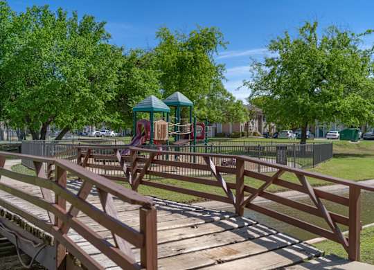A wooden bridge leads to a playground in a park.